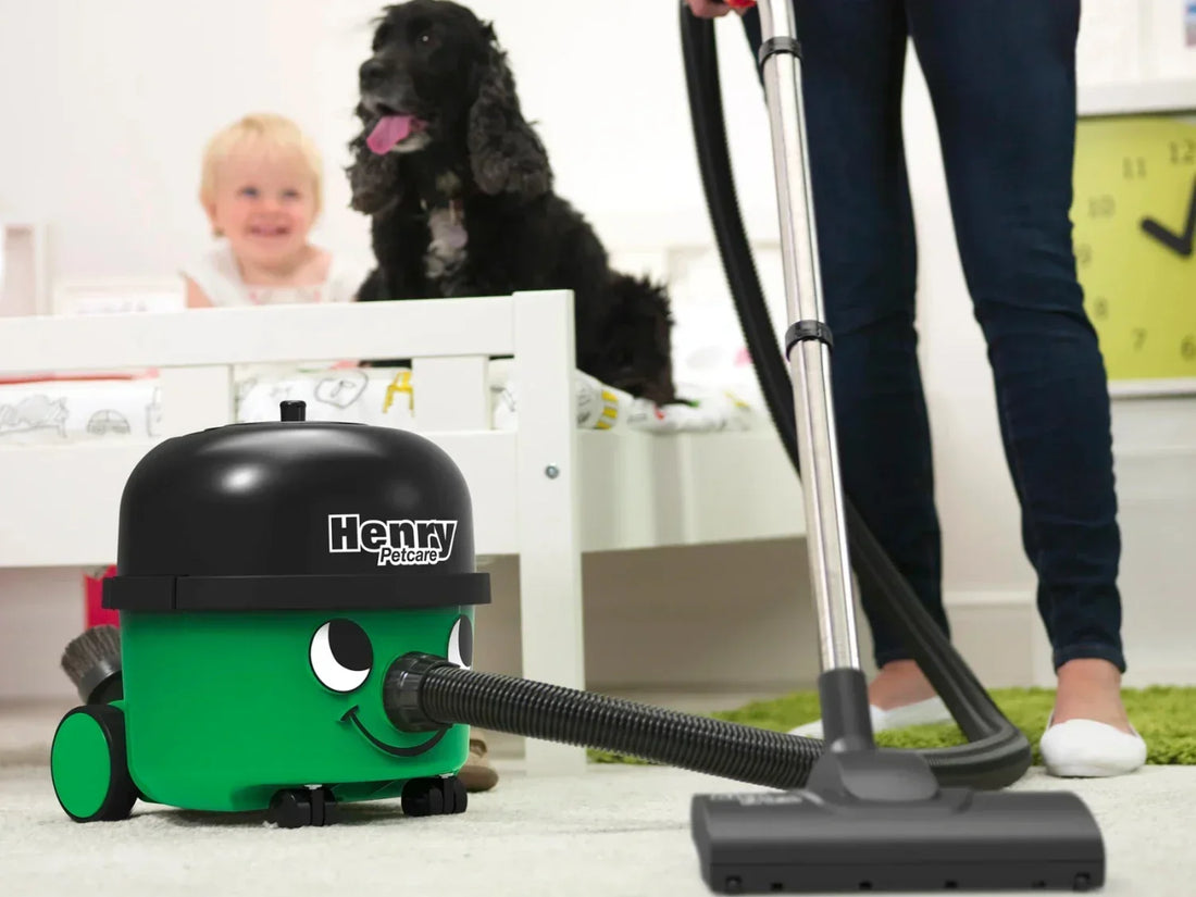 A person using Henry Petcare 160 to vacuum the bedroom floor while a child and a dog sit on the bed. 