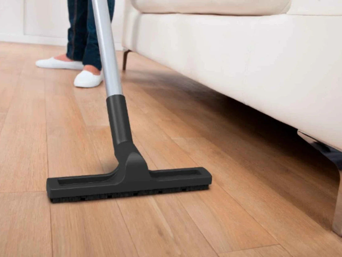 A vacuum for hardwood floors with a soft-bristle hard floor tool cleaning near a cream sofa 