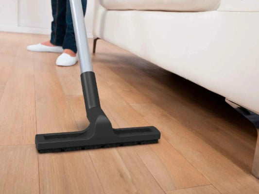 A vacuum for hardwood floors with a soft-bristle hard floor tool cleaning near a cream sofa 
