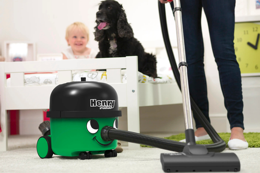 A person using Henry Petcare 160 to vacuum the bedroom floor while a child and a dog sit on the bed. 